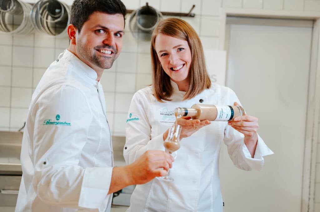 Julia und Mathias Baumgartner lachen freundlich in die Kamera und schenken Likör ein