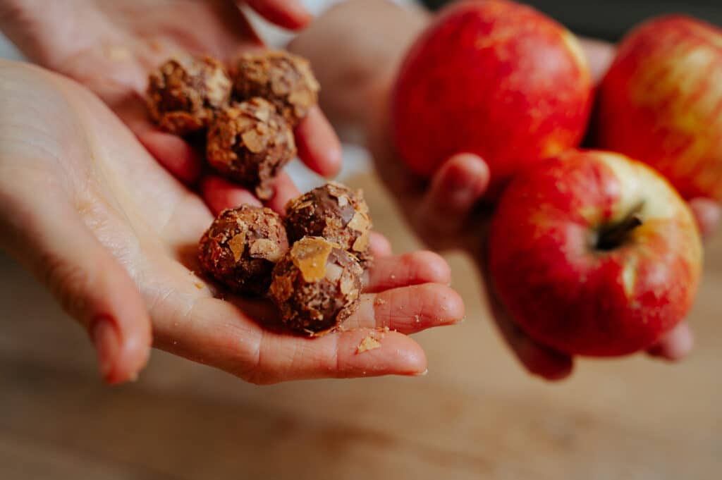 Zwei Hände halten Apfelstrudel Pralinen und zwei Hände halten frische rote Äpfel