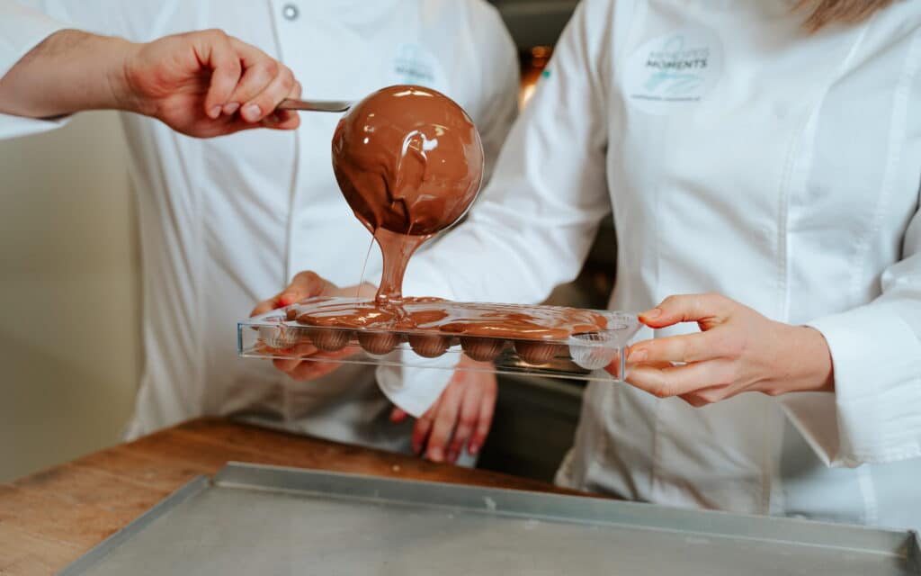 Pralinenform die mit einem Schöpflöffel Schokolade gefüllt wird