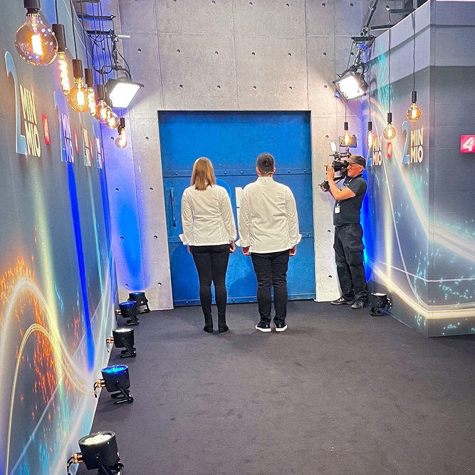 Julia und Mathias Baumgartner stehen mit dem Rücken zur Kamera und warten, dass die Tür zu den Juroren bei 2 Minuten 2 Millionen sich öffnet