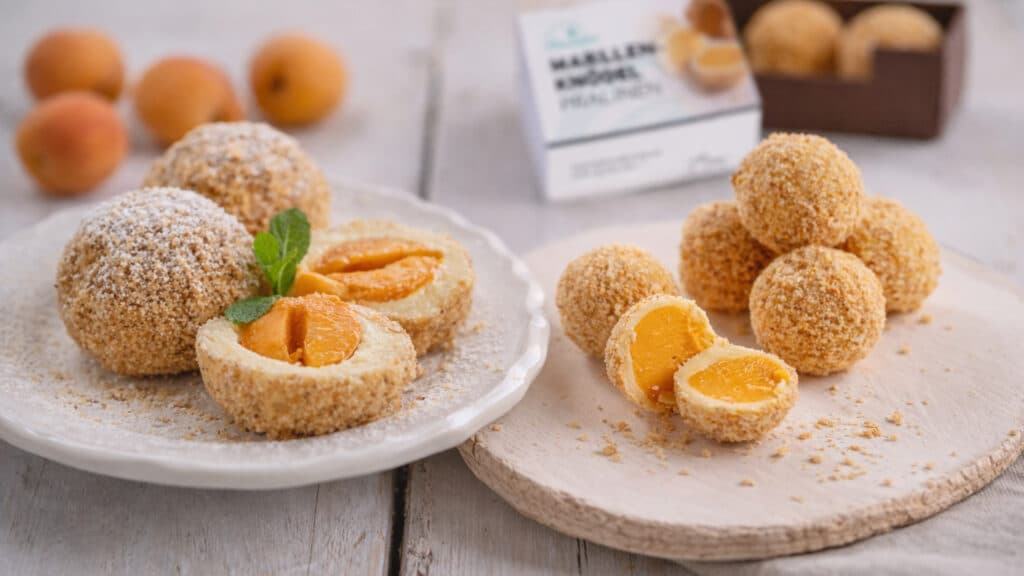 Zwei Teller auf einem Holztisch - eines mit Marillenknödel und eines mit Marillenknödel Pralinen. Heller freundlicher Fotostil