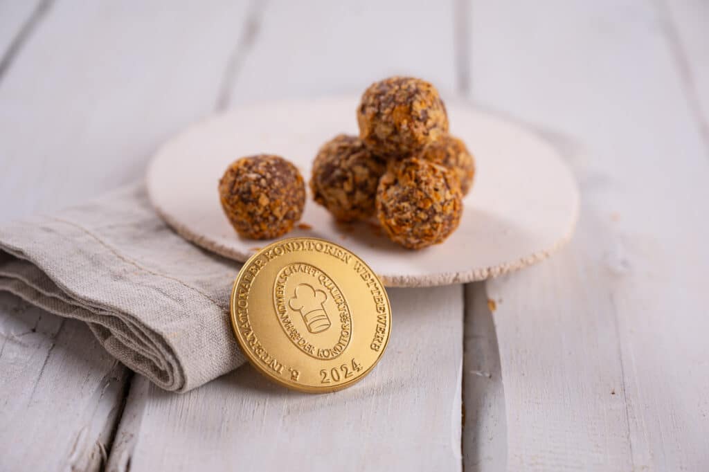 Apfelstrudelpraline auf einem Teller und im Vordergrund die Goldmedaille vom internationalen Konditorenwettbewerb