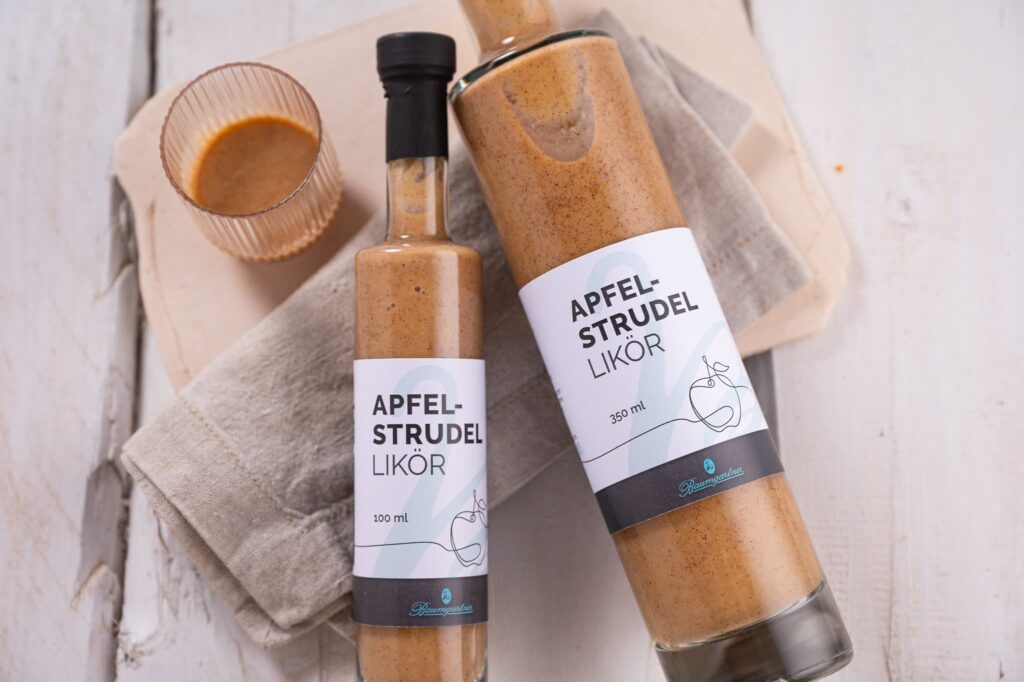 Apfelstrudel Likör in der Flasche liegen auf einem schönen Holzuntergrund daneben ein Glas gefüllt mit dem Likör
