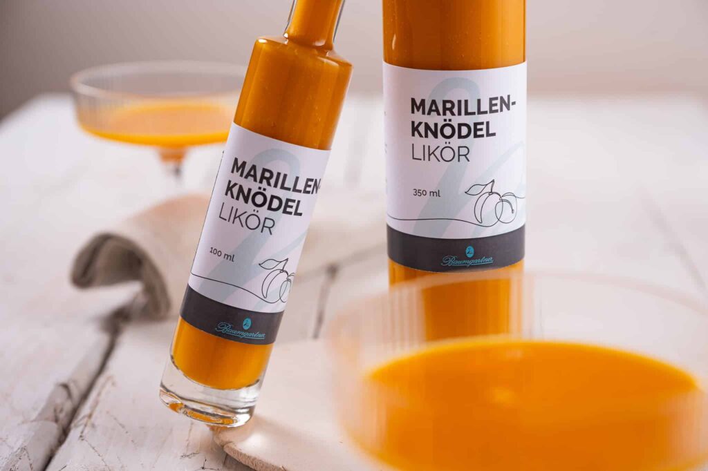 Flaschen Marillenknödellikör aneinander gelehnt und davor ein Glas mit Likör eingeschenkt